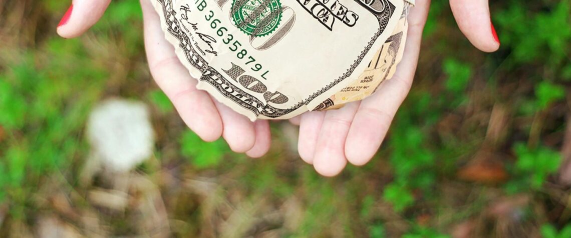 Hands holding crumpled money outdoors, symbolizing charity and financial support.